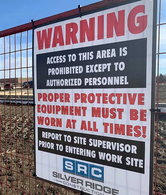 Site safety warning sign on a construction fence